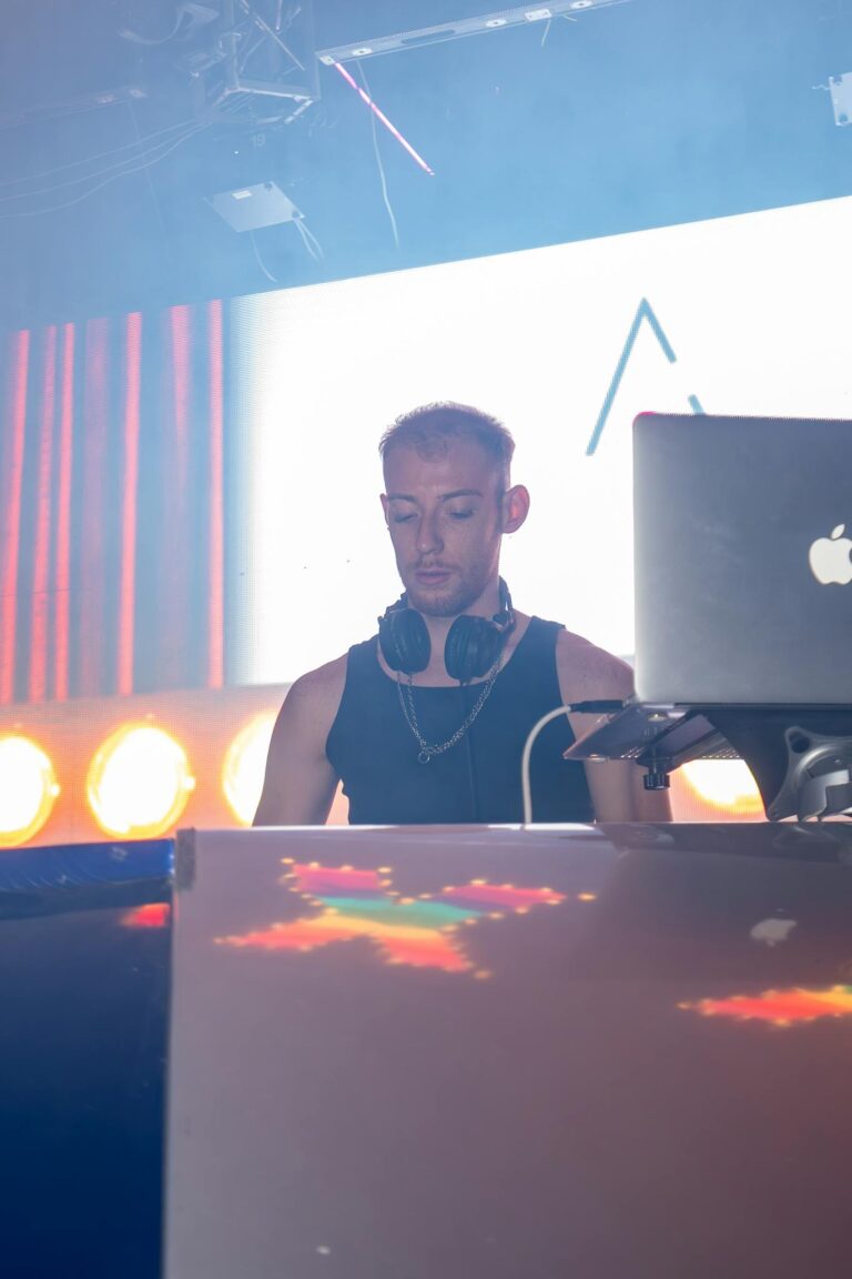A DJ playing music at a vibrant nightclub with colorful lights and a crowd.
