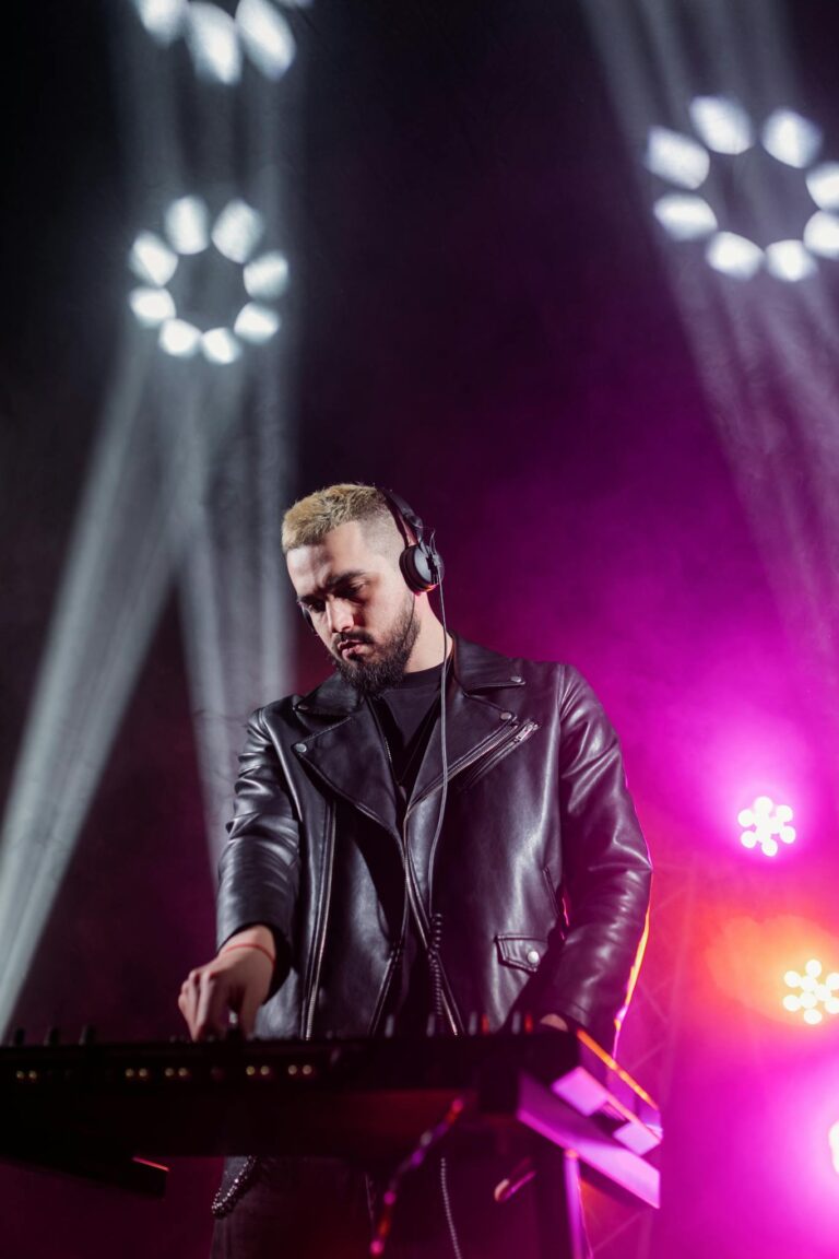 DJ in leather jacket performs under dynamic stage lights at night event.